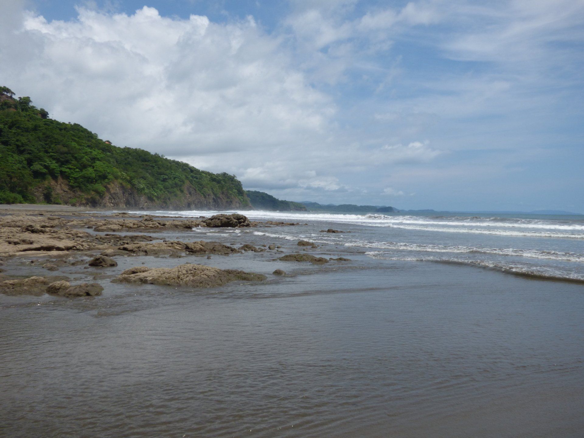 A beach with waves crashing against the rocks on a sunny day