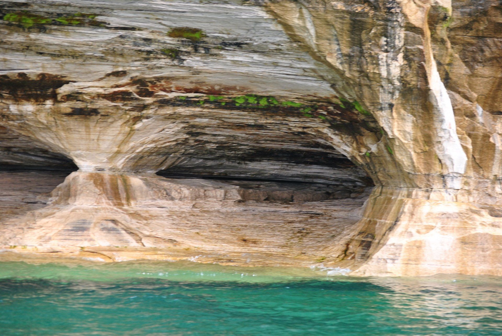 A waterfall is coming out of a cave in the rocks next to a body of water.