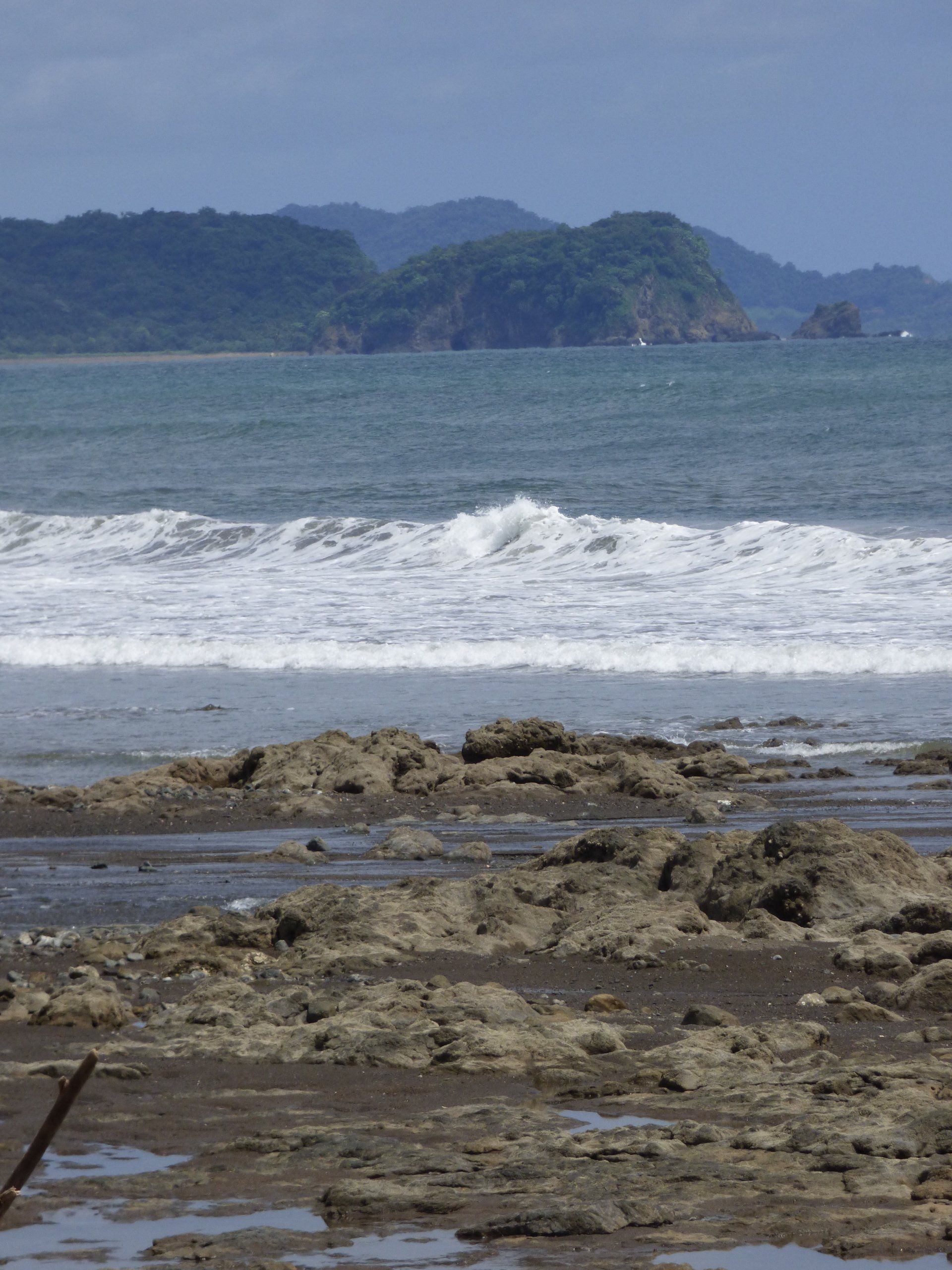 A beach with rocks in the foreground and mountains in the background