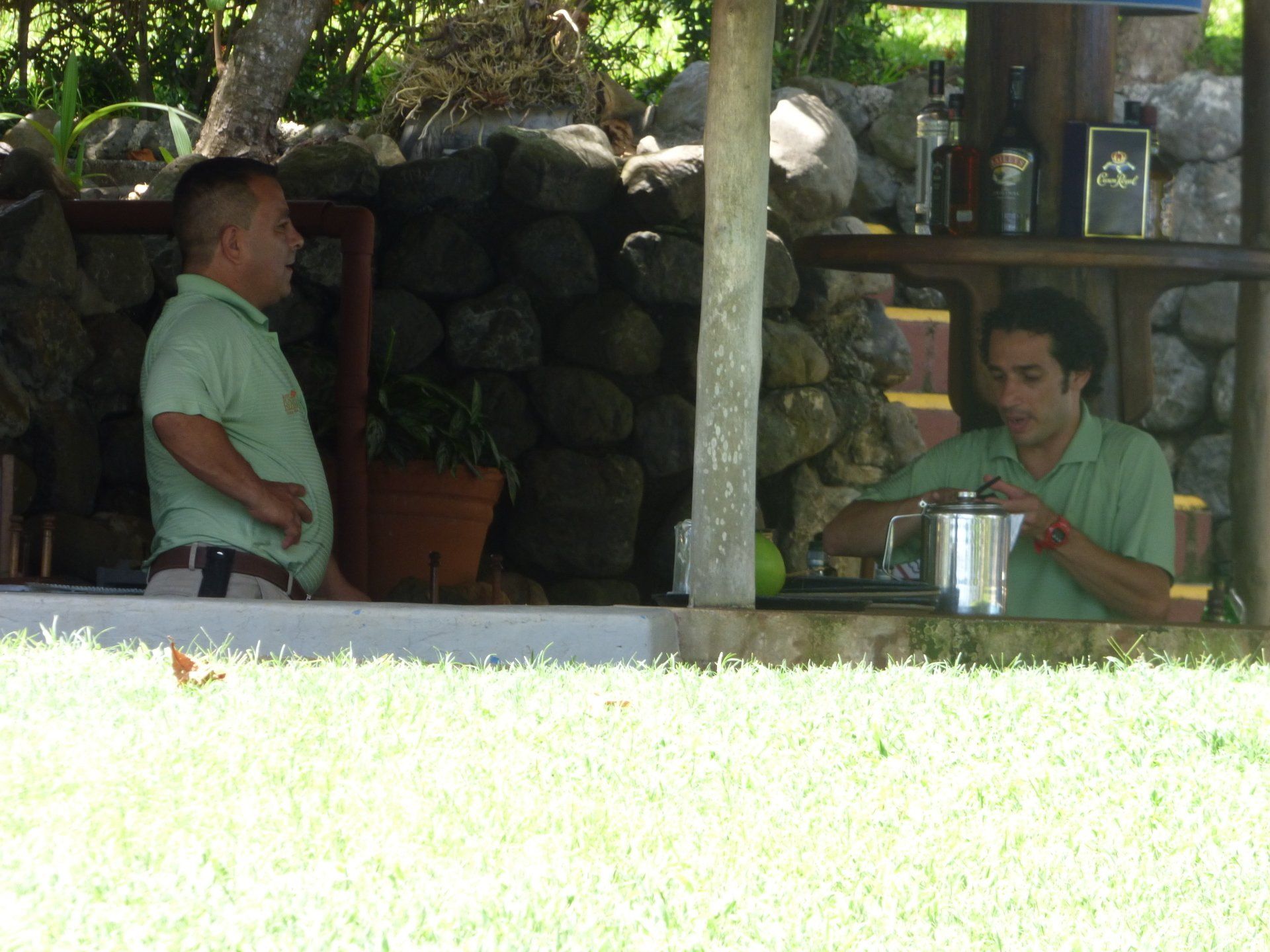 Two men are sitting in front of a stone wall talking