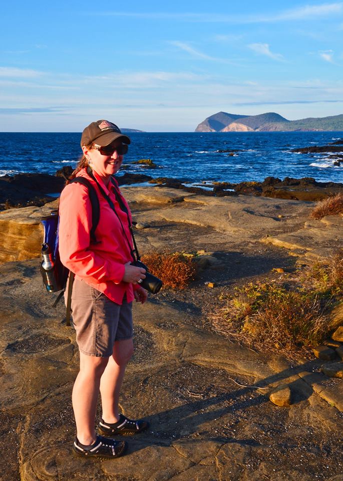 A woman is standing on a rocky cliff overlooking the ocean.