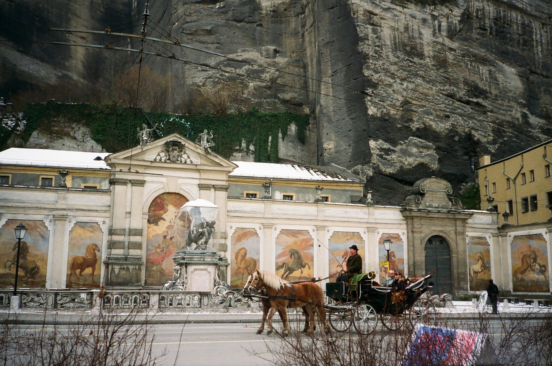 A man is riding a horse drawn carriage in front of a building