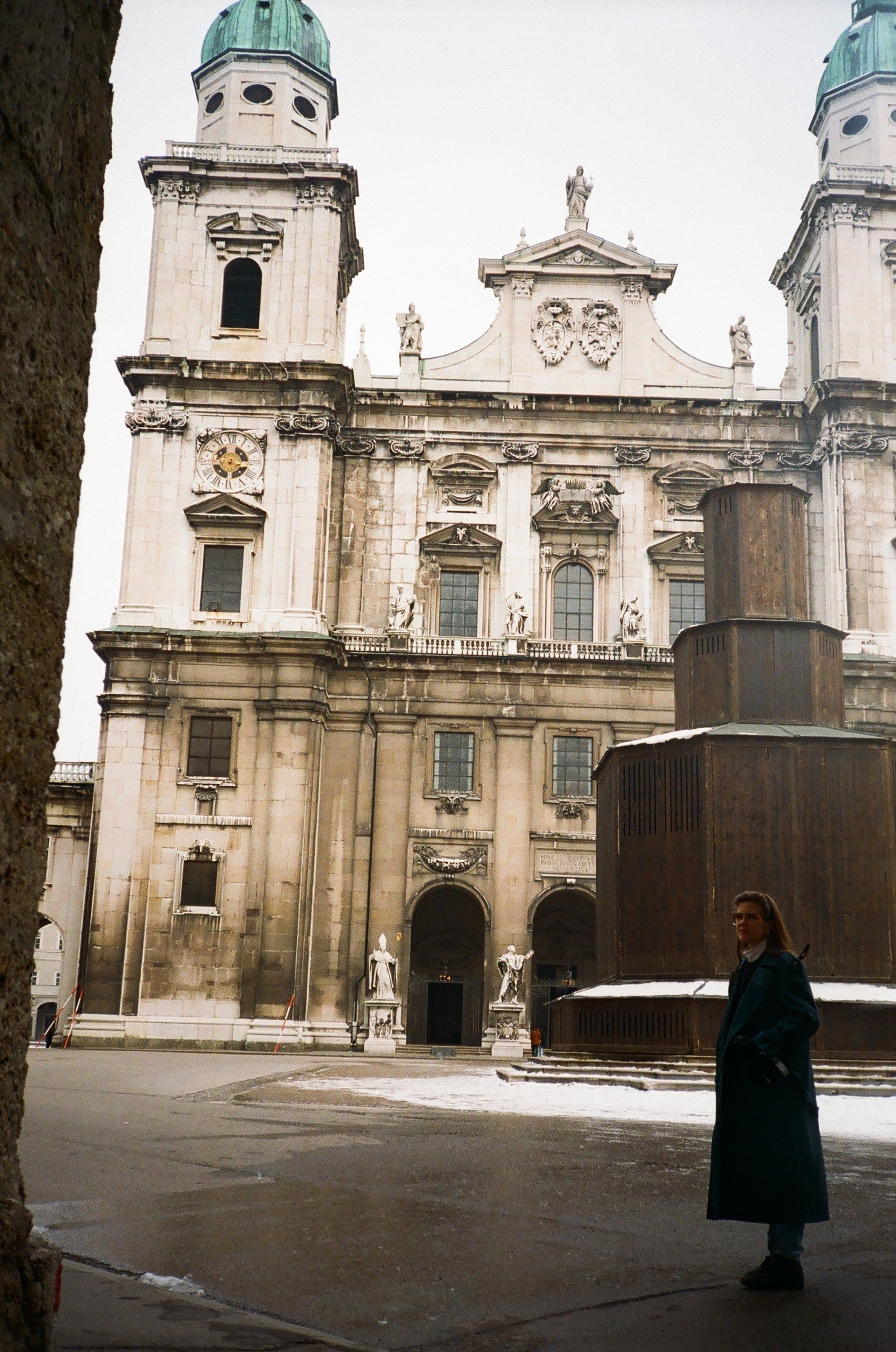 A woman in a black coat stands in front of a large building
