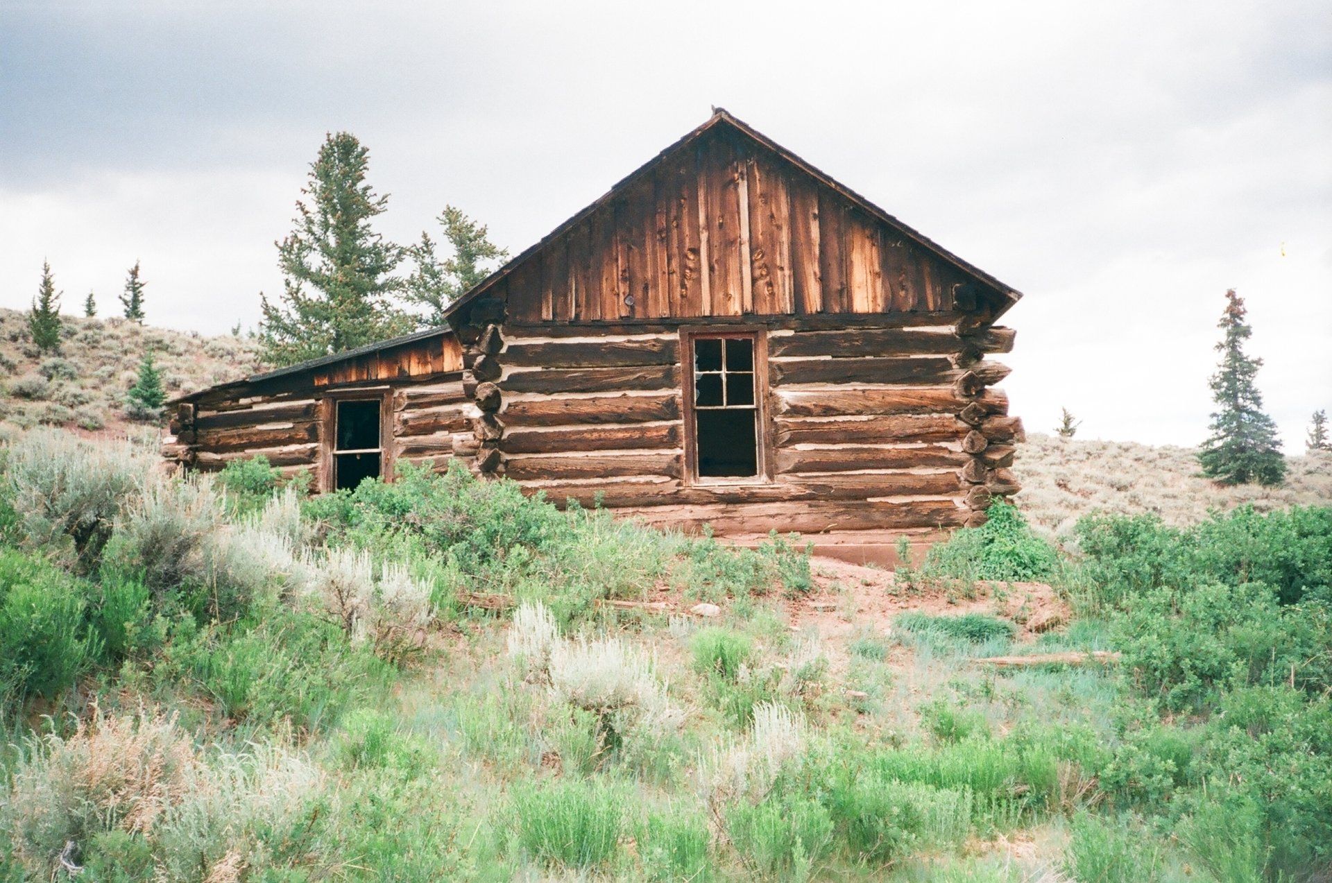 An old log cabin is sitting in the middle of a grassy field.