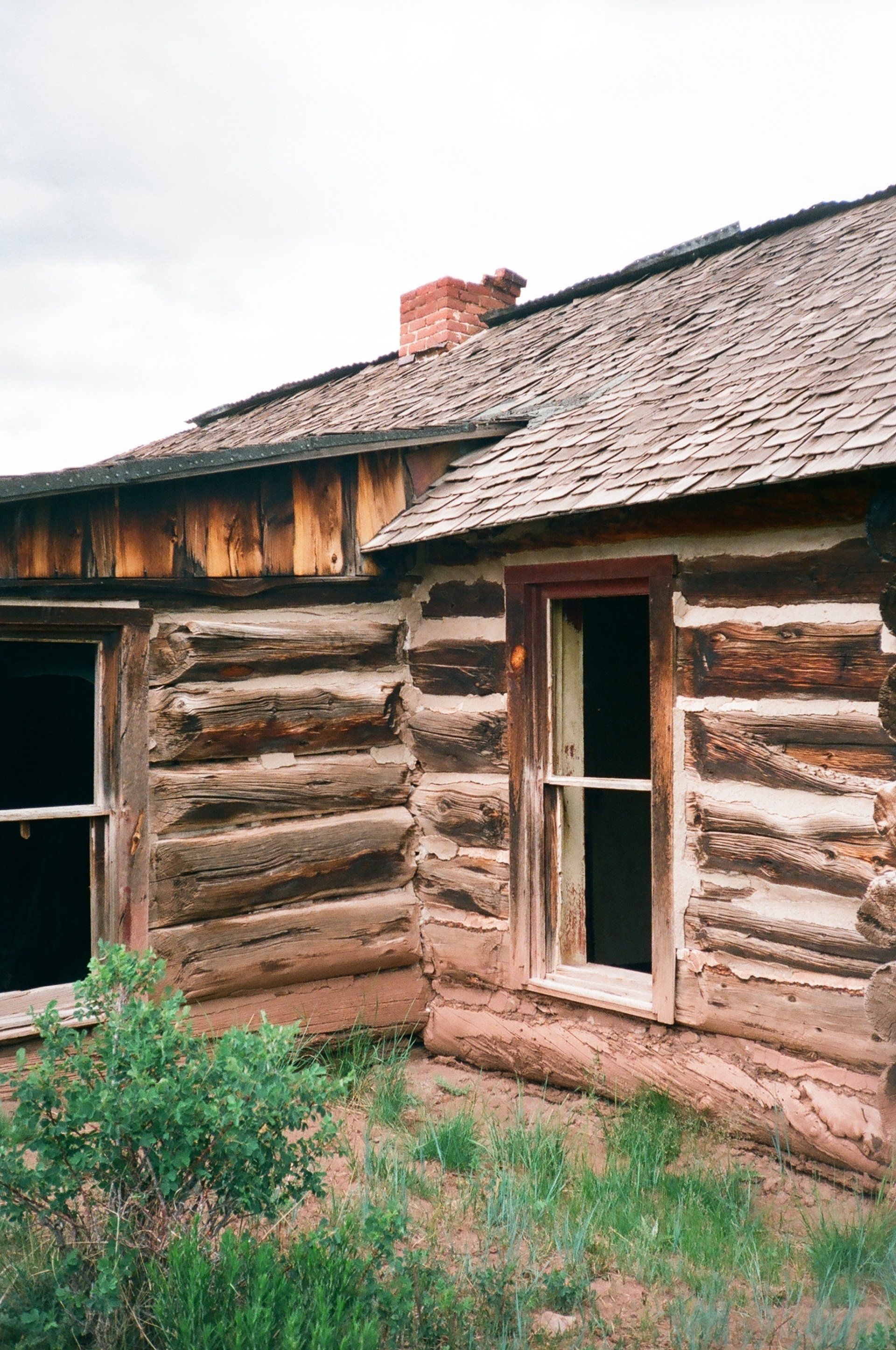 A log cabin with two windows and a chimney on the roof.