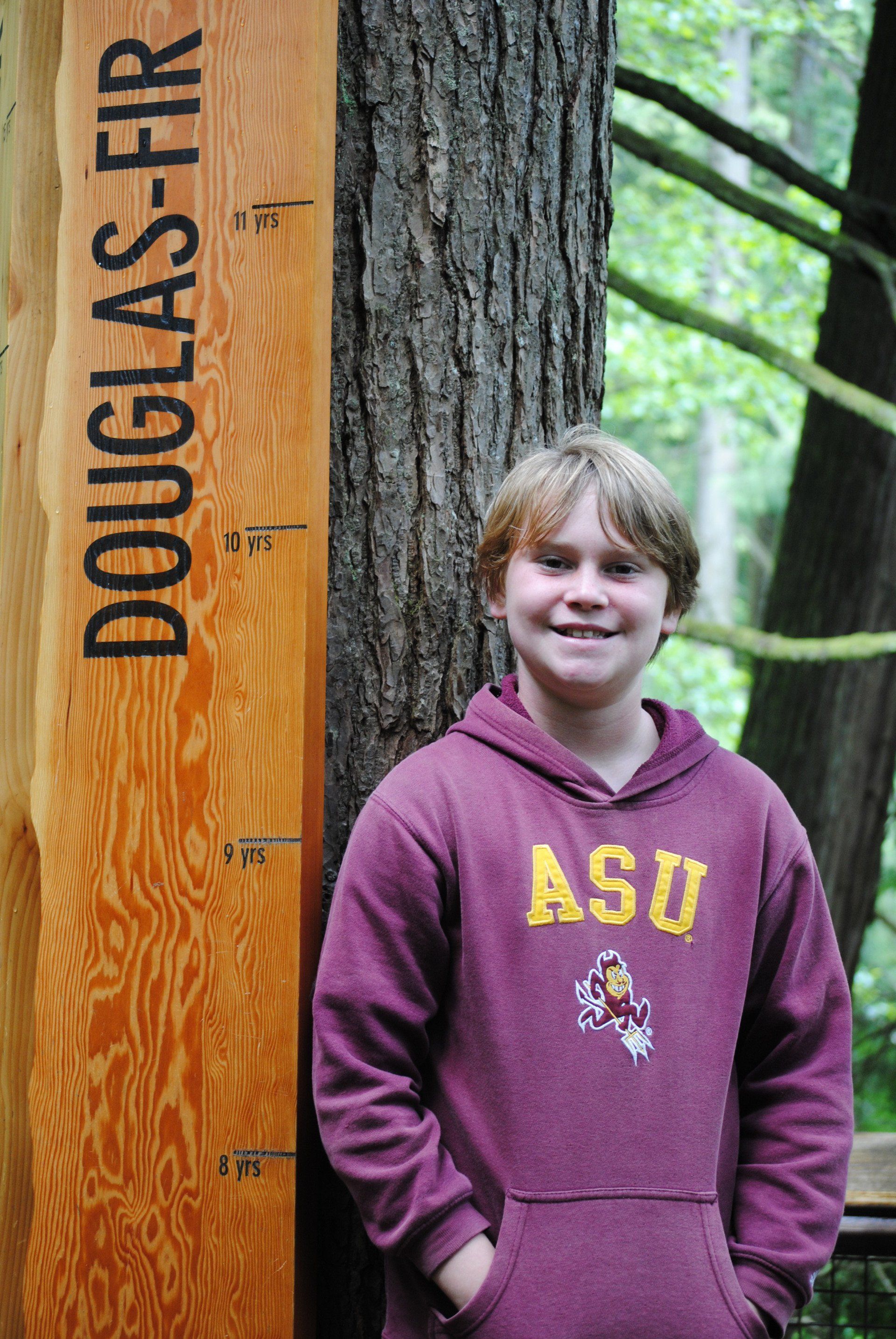 A young boy is standing next to a wooden sign that says douglas fir