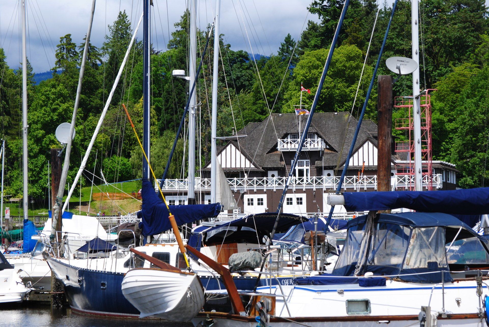 A row of boats are docked in a marina with a house in the background