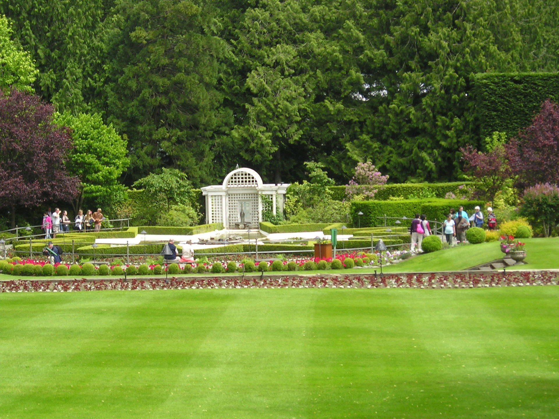 A group of people are walking in a park with a gazebo in the background