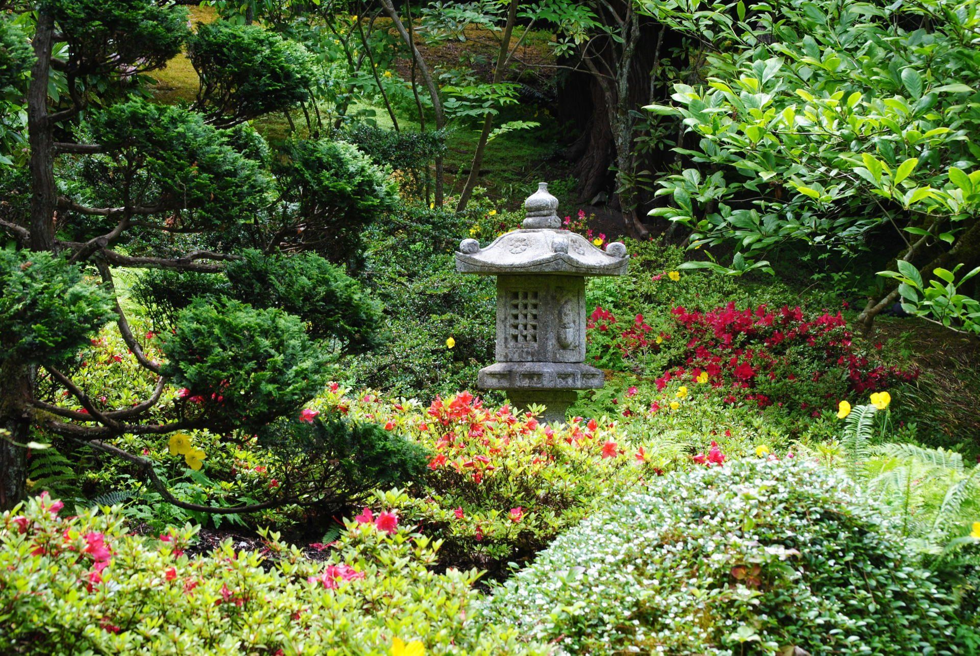 A stone lantern is in the middle of a garden surrounded by trees and flowers.