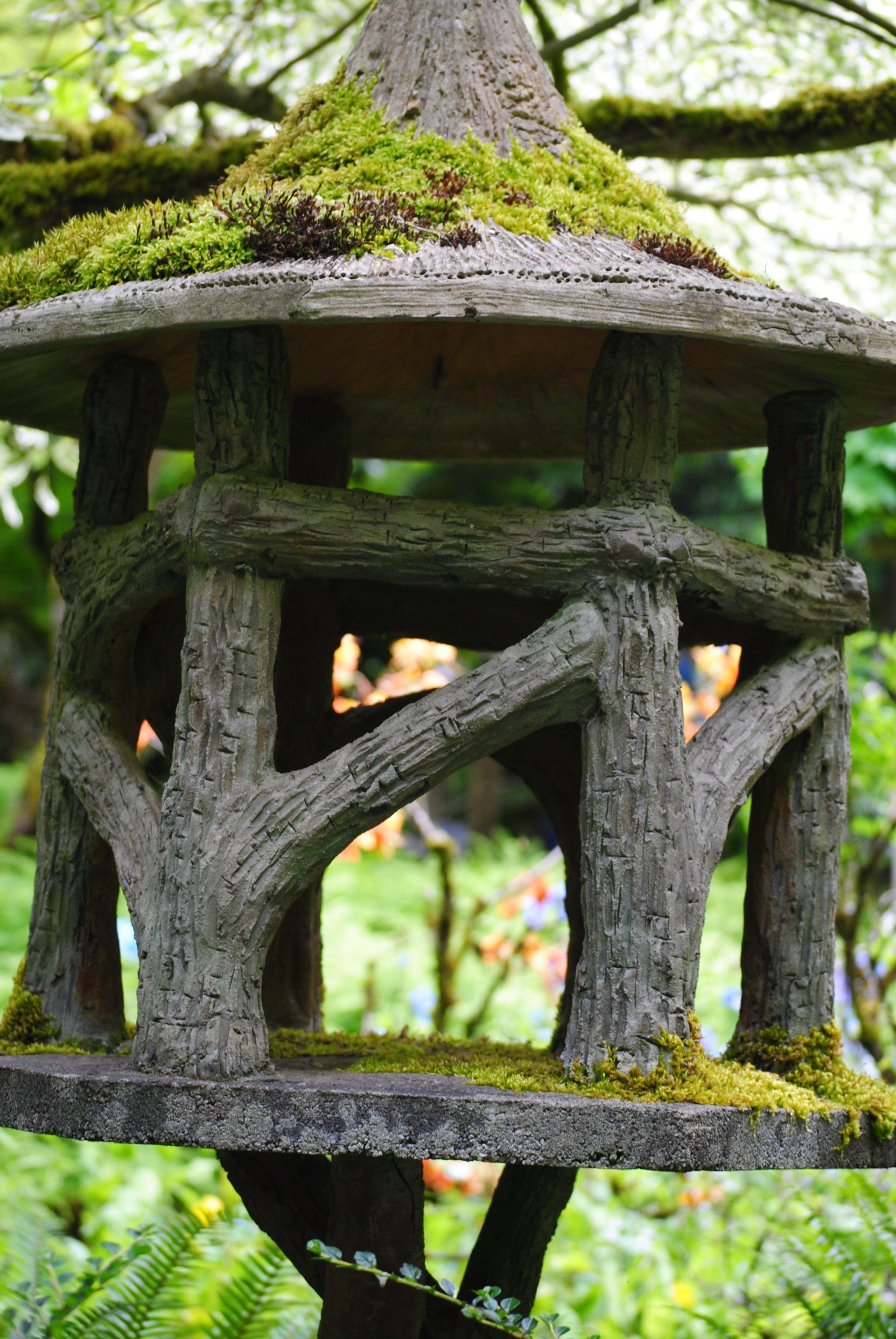 A wooden birdhouse with moss on top of it is hanging from a tree.