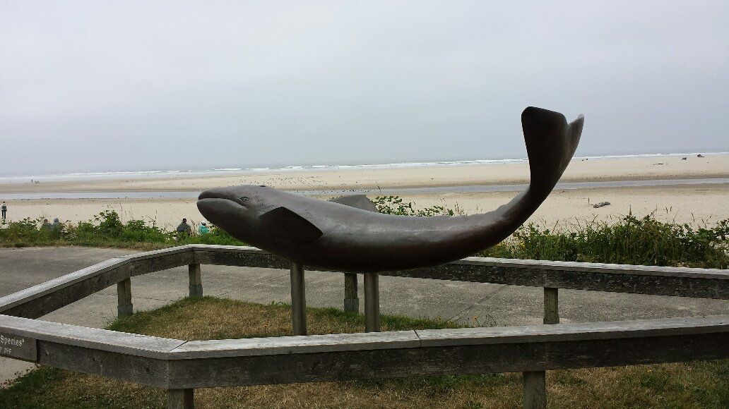 A statue of a whale is sitting on top of a fence in front of a beach.