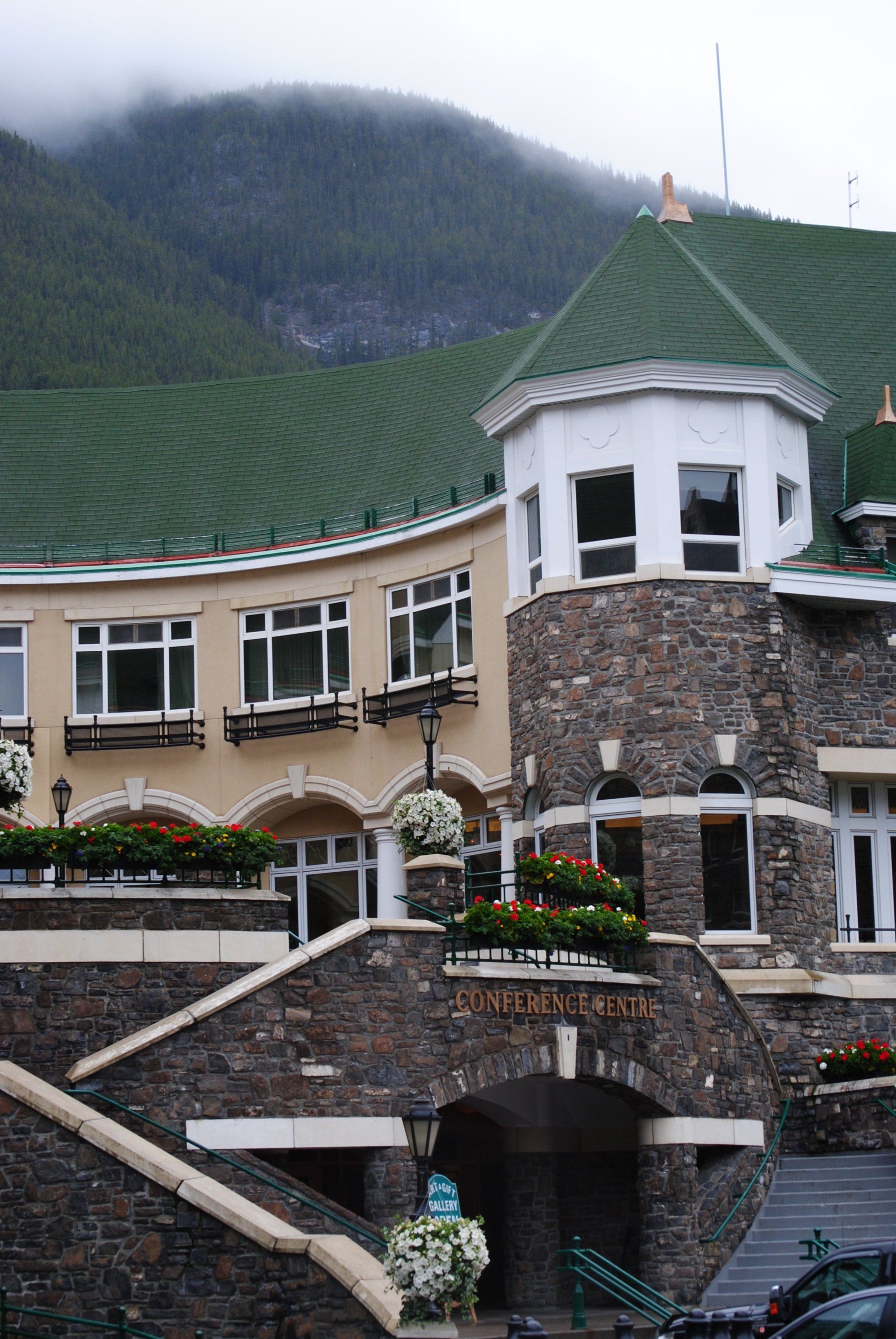 A large stone building with a green roof is surrounded by mountains.
