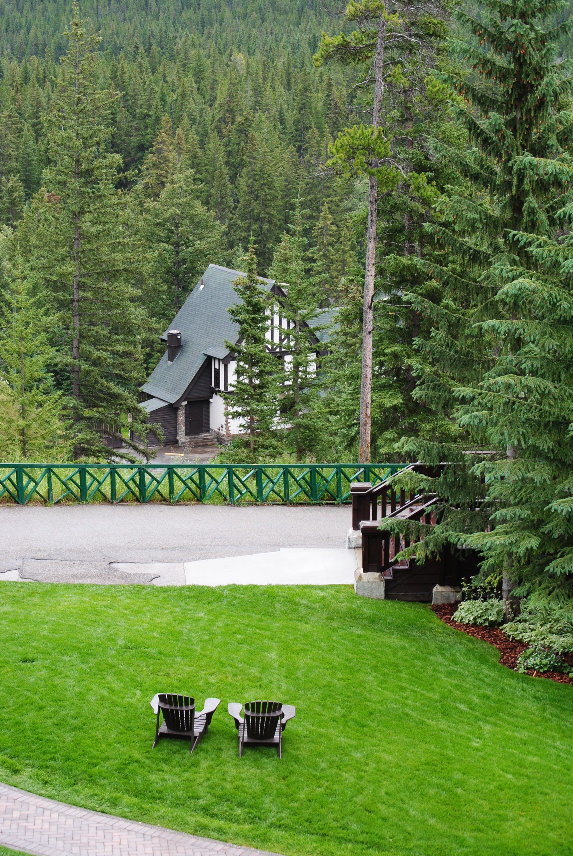 Two chairs are sitting on a lush green lawn in front of a house surrounded by trees.