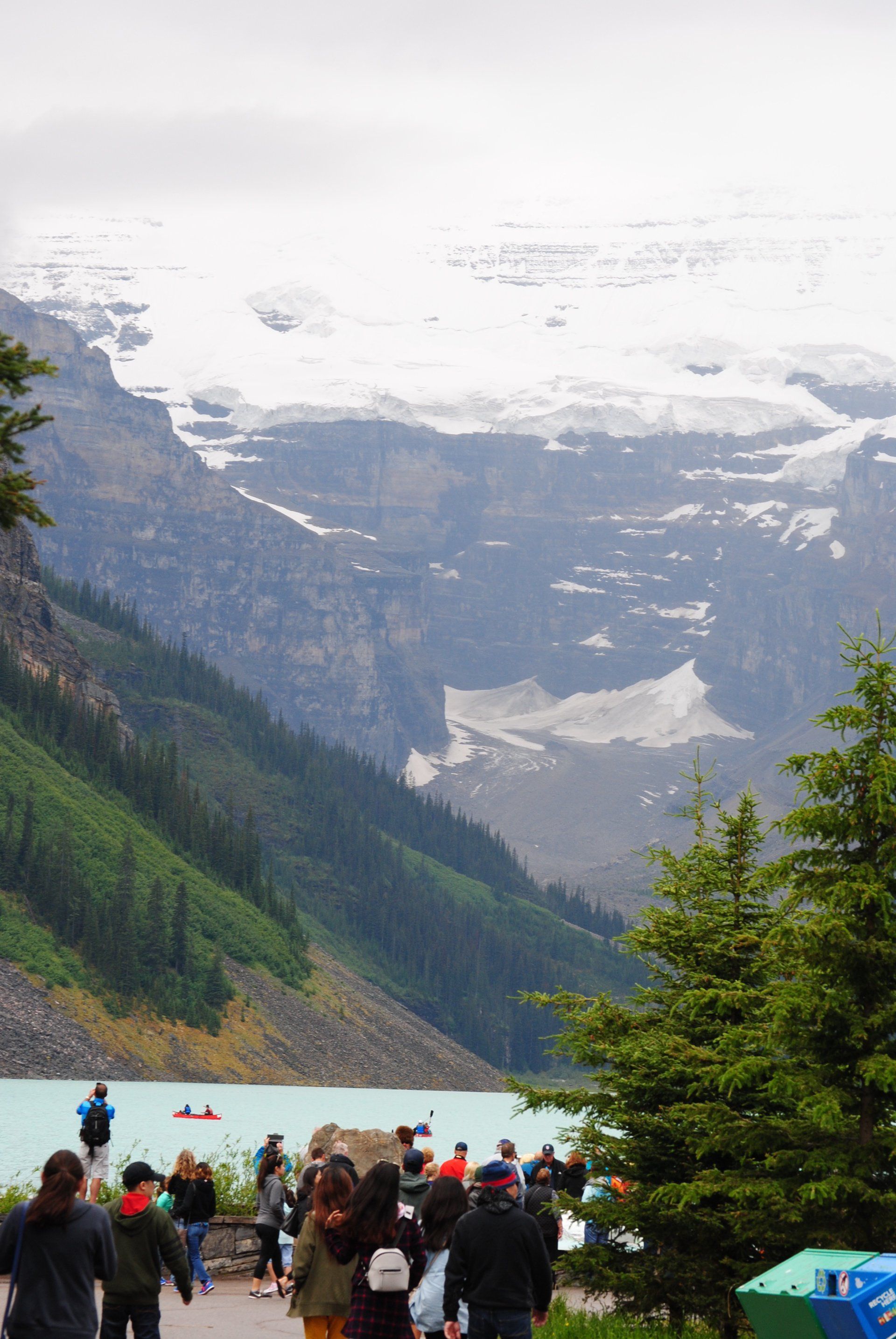 A group of people are walking down a path next to a lake with mountains in the background.