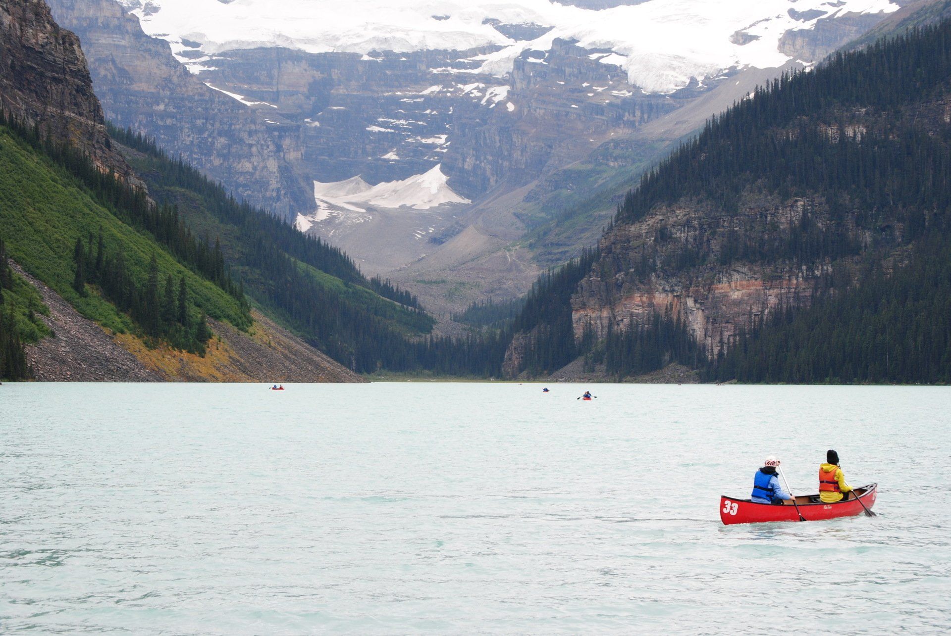 Two people in a red canoe on a lake with mountains in the background