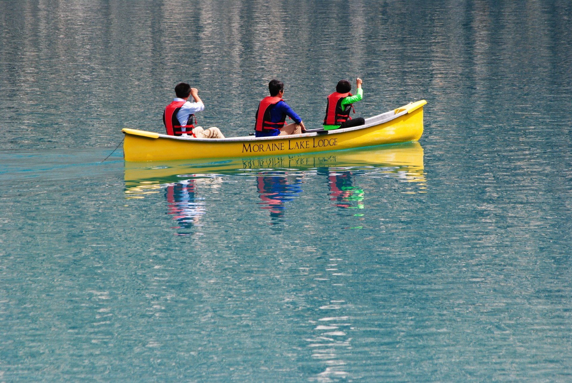 Three people are in a yellow canoe on a lake