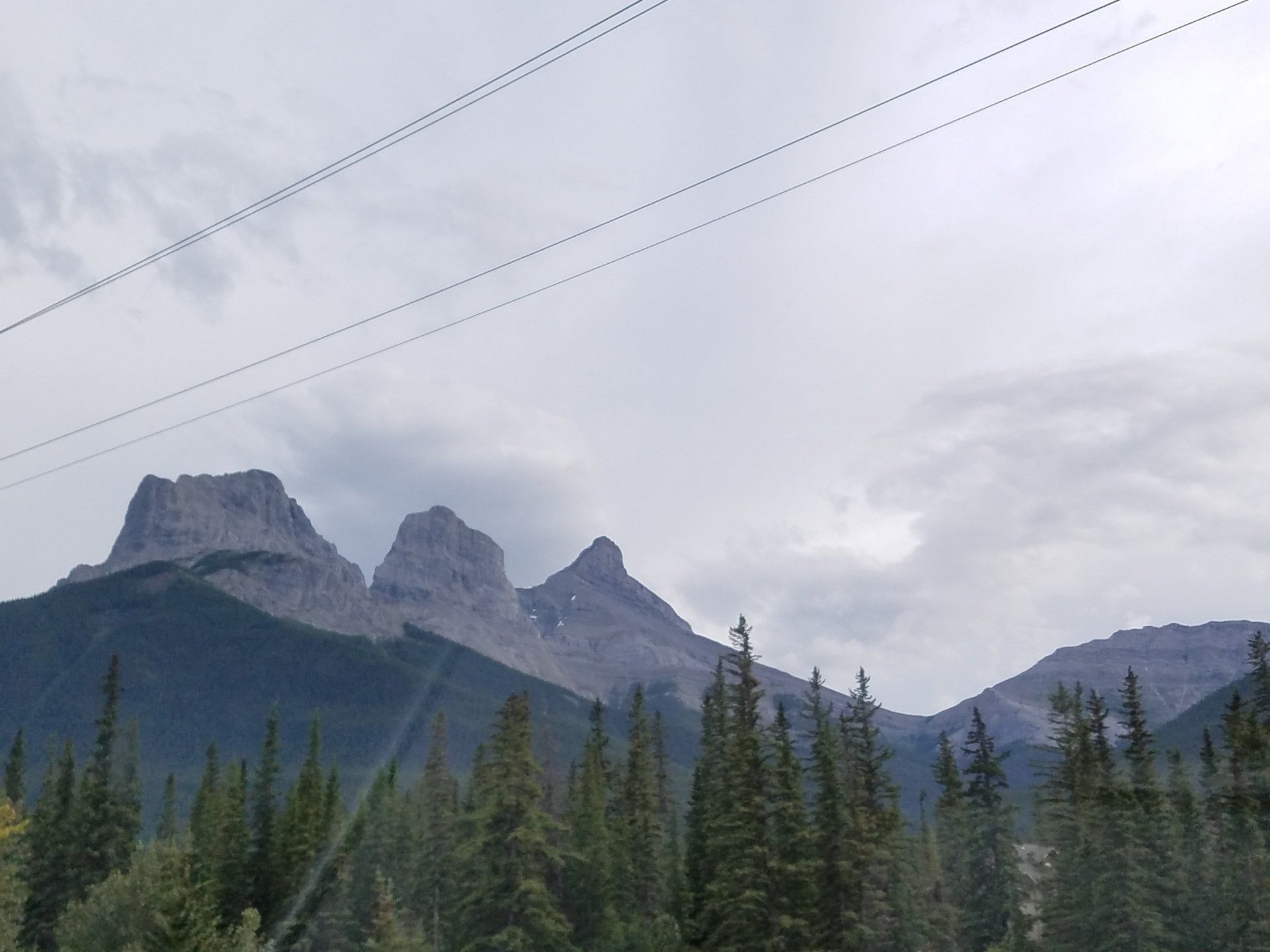 A mountain range with trees and power lines in the foreground