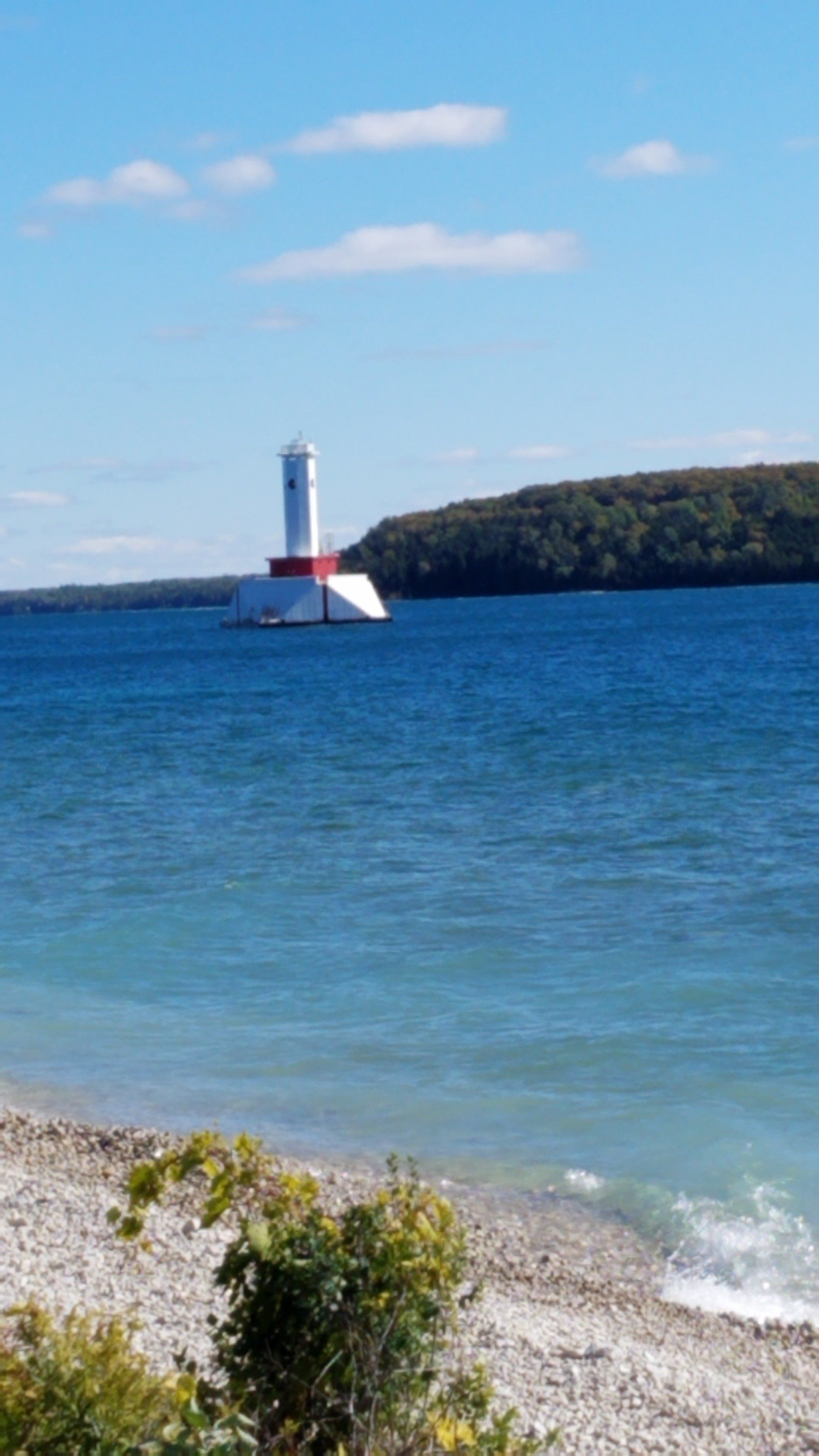A lighthouse is sitting on a small island in the middle of a body of water.