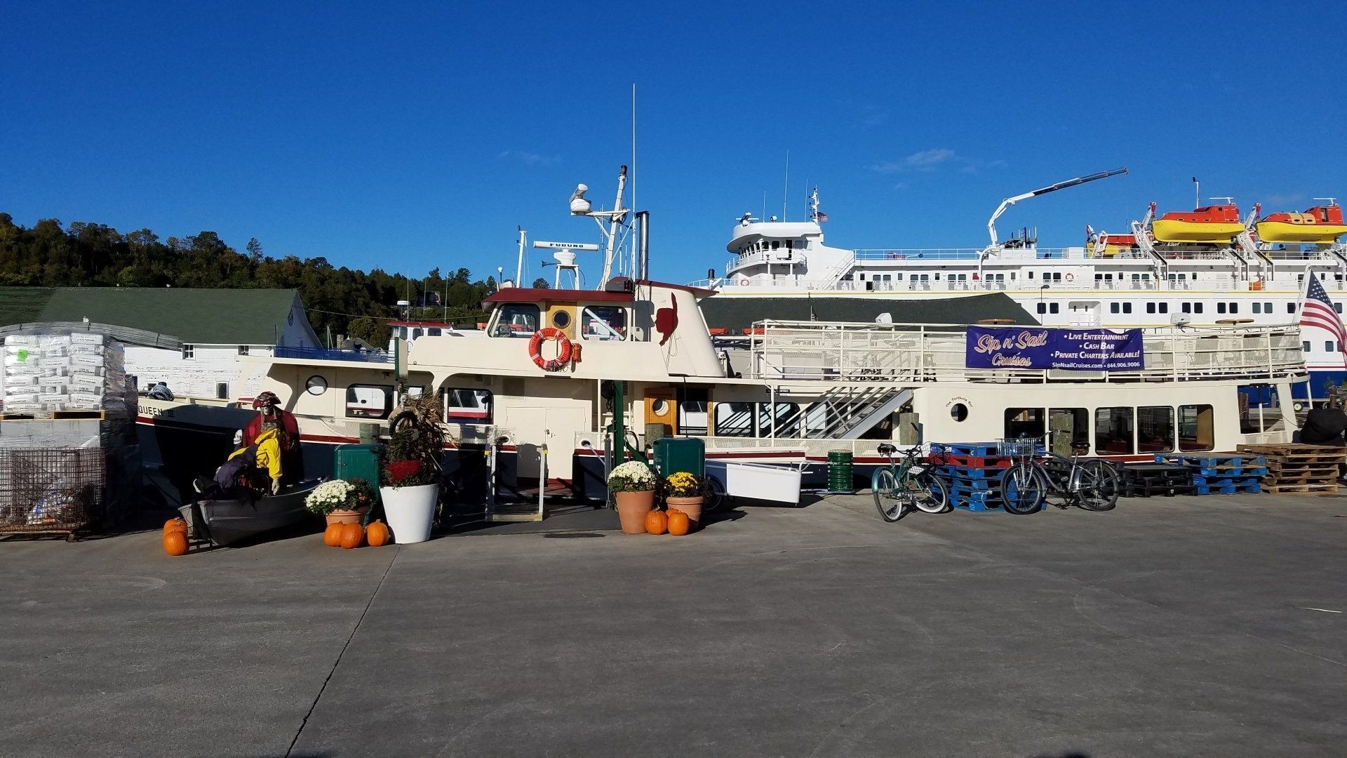 A large ship is docked at a harbor with pumpkins and flowers in front of it.