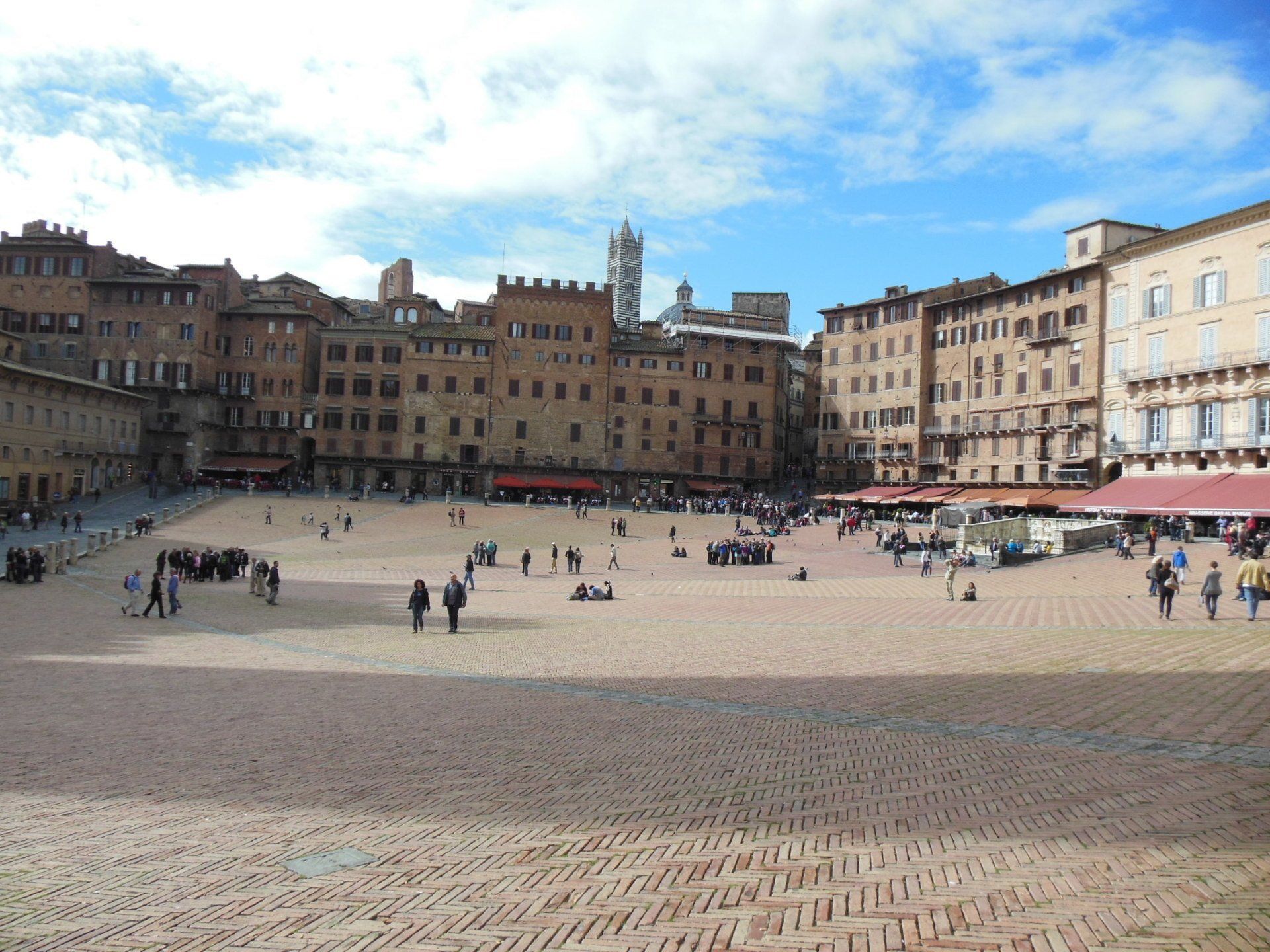 A group of people are walking in a large square surrounded by buildings