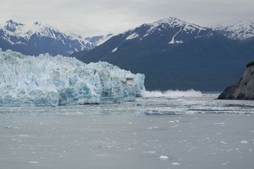 A large iceberg in the middle of a body of water with mountains in the background.