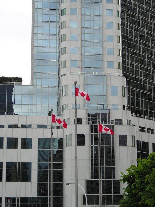 Two canadian flags are flying in front of a tall building