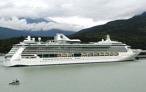 A cruise ship is docked in the water with mountains in the background