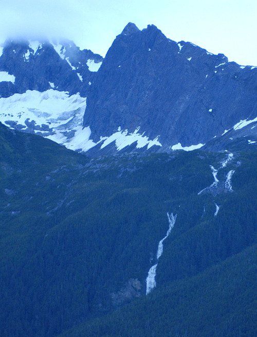 A mountain covered in snow with a waterfall in the foreground