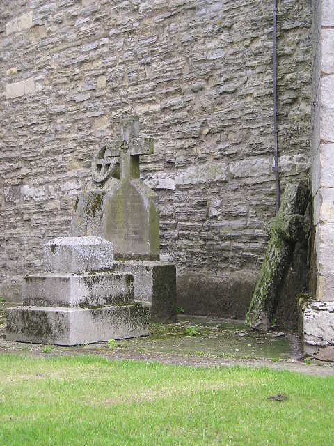 A stone cross is sitting in front of a stone wall.