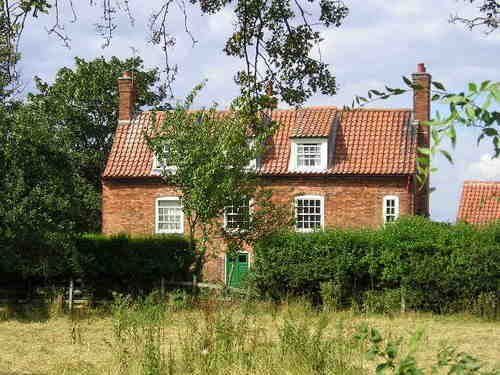 A large brick house with a green door is surrounded by trees and bushes.
