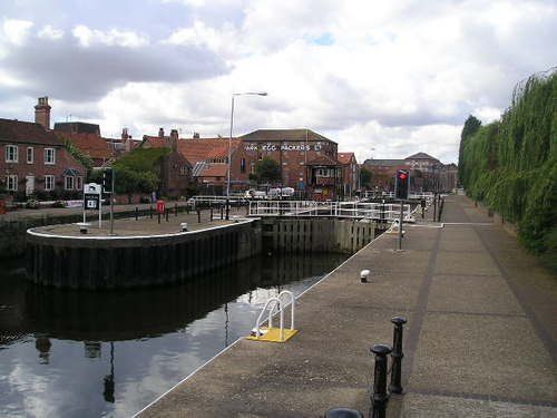 A concrete walkway along a body of water with buildings in the background