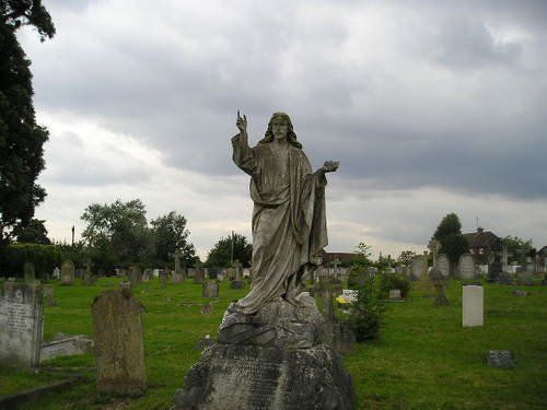 A statue of jesus in a cemetery with a cloudy sky