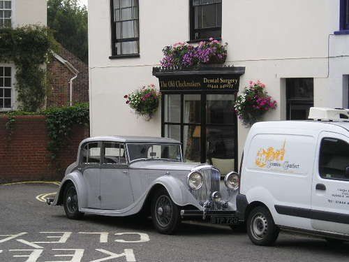 A silver car is parked in front of a white building