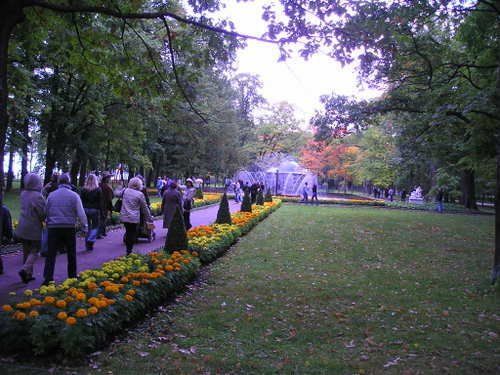 A group of people are walking through a park with a fountain in the background
