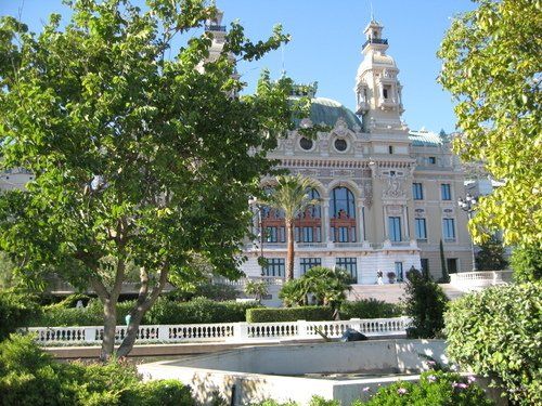 A large building with a clock tower is surrounded by trees and bushes