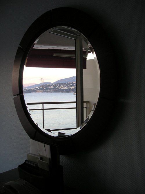 A round mirror shows a balcony overlooking the ocean