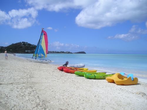 A row of kayaks and a sailboat on a beach