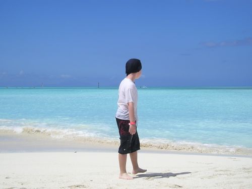 A boy is standing on a beach looking at the ocean