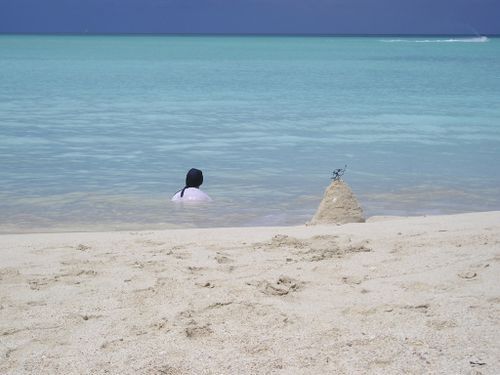 A person is swimming in the ocean near a sand castle