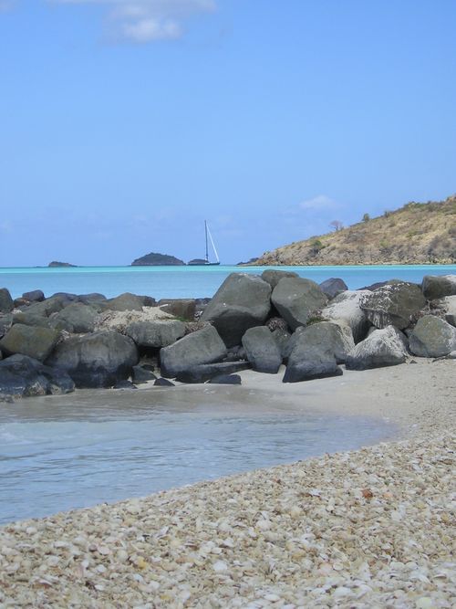 A rocky beach with a sailboat in the distance
