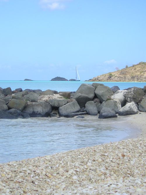 A rocky beach with a sailboat in the distance