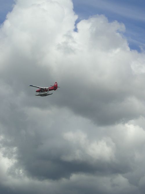 A red plane is flying through a cloudy sky