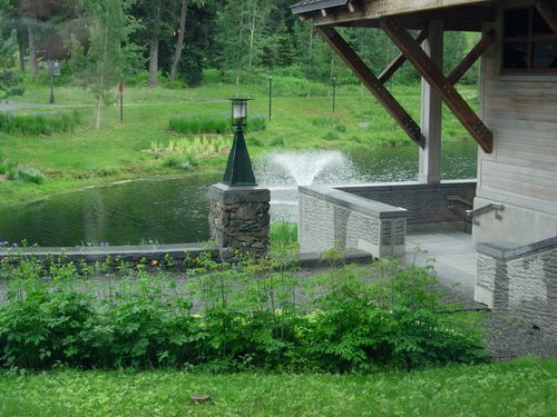 A pond with a fountain in the middle of it and a building in the background.