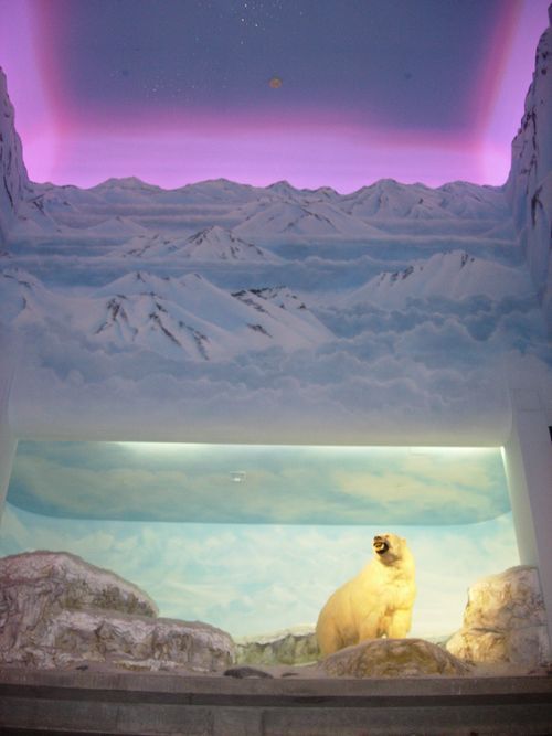 A polar bear is sitting in front of a painting of mountains