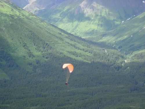 A person is parasailing over a lush green mountain range.