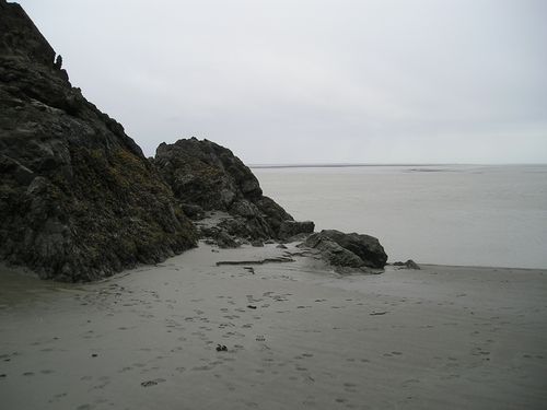 A rocky cliff on a beach with a large body of water in the background