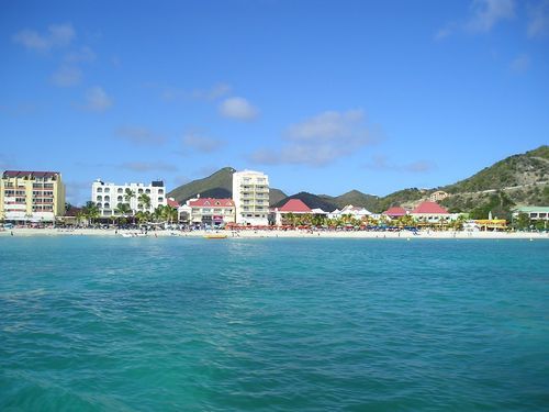 A beach with buildings and mountains in the background and a body of water in the foreground.
