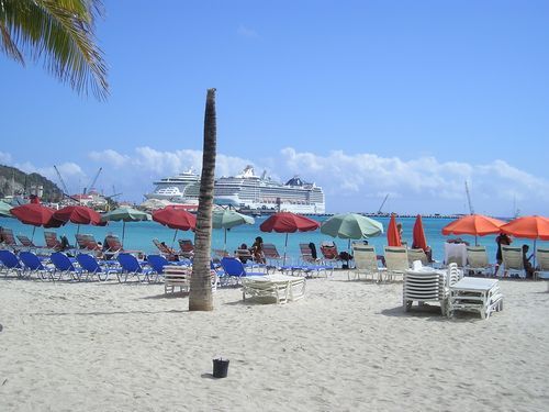 A beach with umbrellas and chairs and a cruise ship in the background