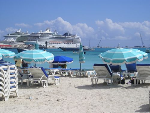 A beach with chairs and umbrellas and a cruise ship in the background