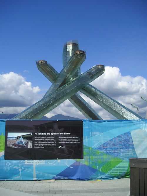 A large sculpture is behind a blue fence with a sign on it